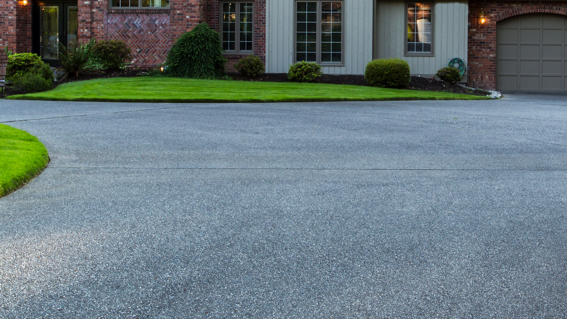 Curved brick driveway in front of a house with trimmed green lawn and garage