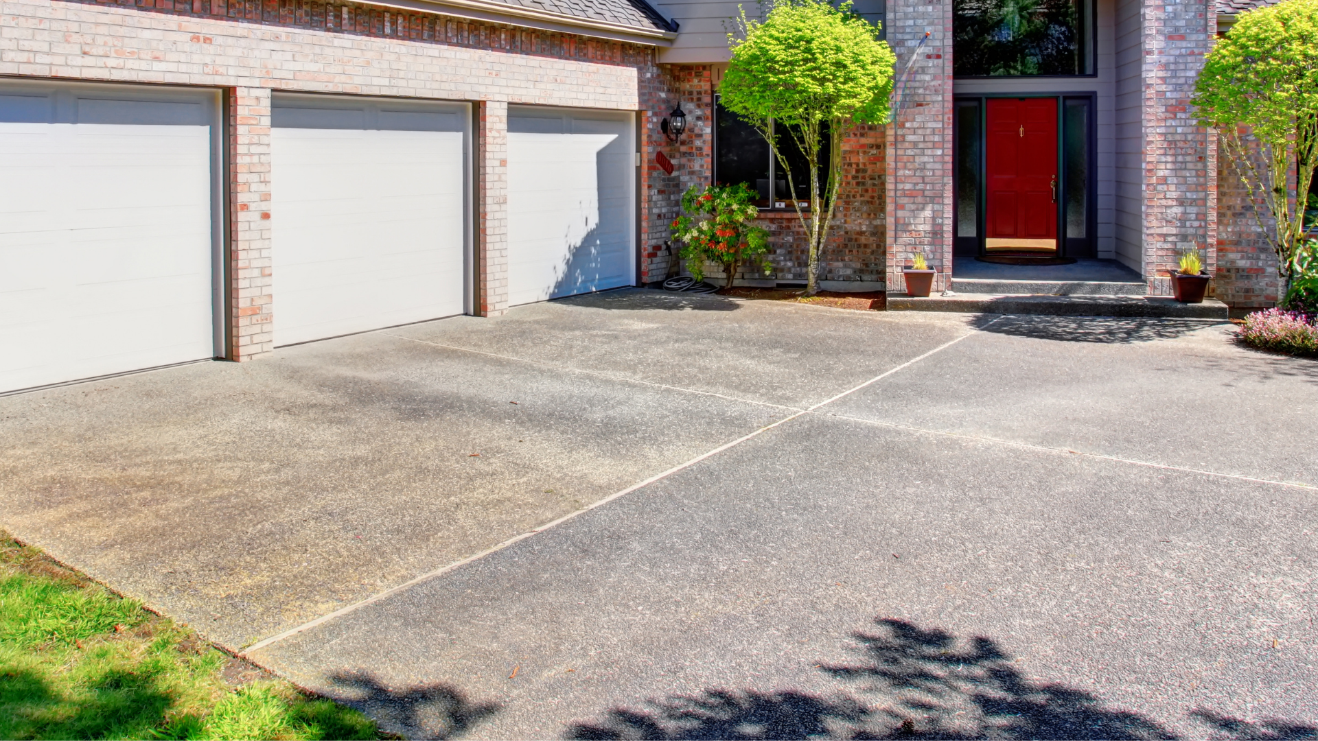 Suburban house with three garage doors, a red front door, and a sunlit driveway