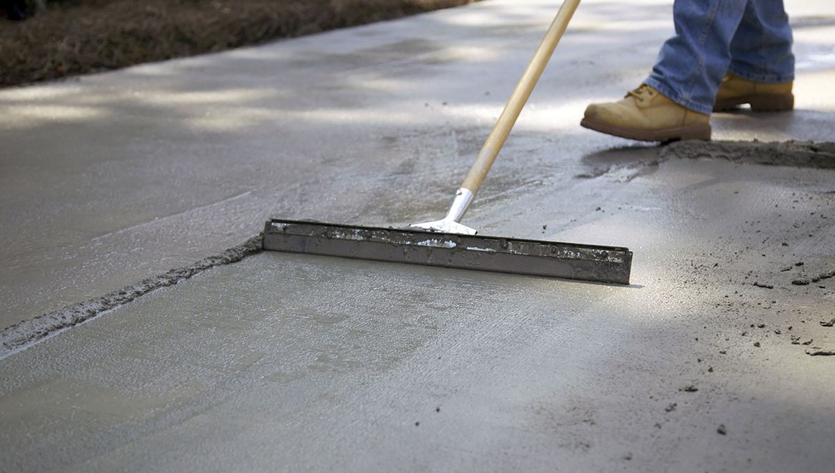 Worker smoothing wet concrete with a long squeegee on a driveway or road surface
