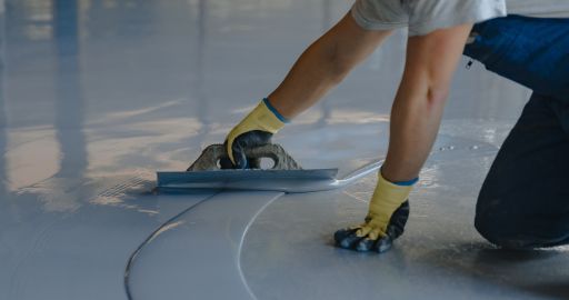 Worker smoothing wet concrete with a trowel on a floor