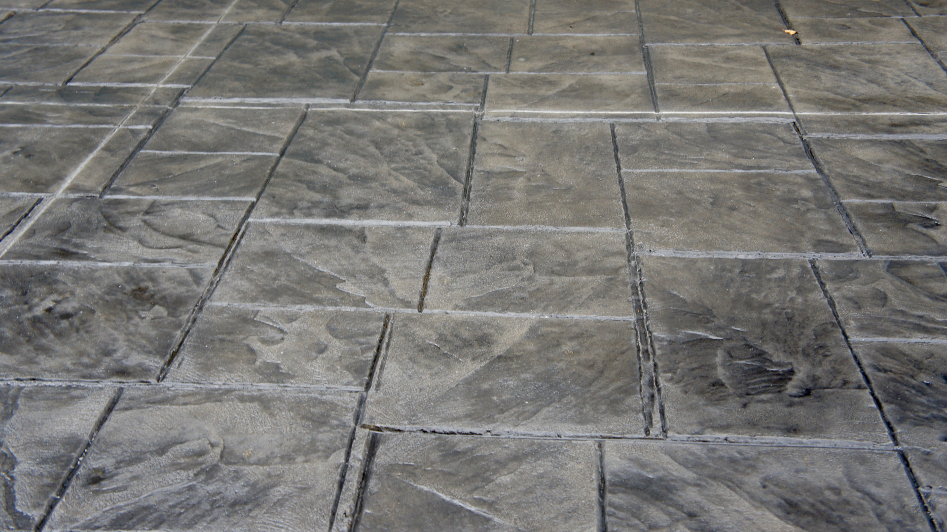 Gray stamped concrete pavement with a grid-like stone pattern and visible cracks.