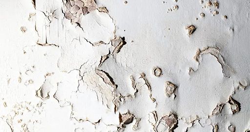 Peeling white paint on a weathered wall with cracked, flaking patches