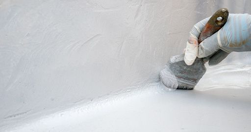 Gloved hand painting a white wall with a roller inside a bright room