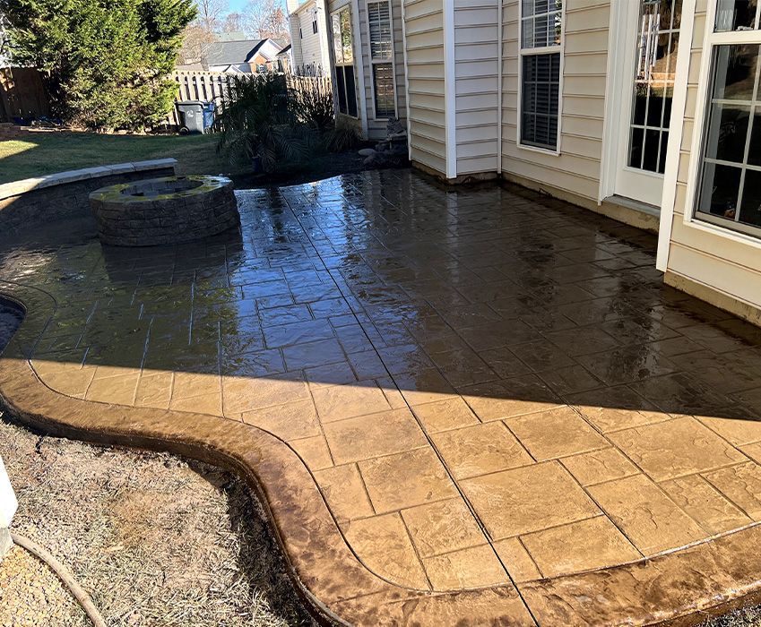 Stone patio beside a house, dark wet surface with water reflecting sunlight
