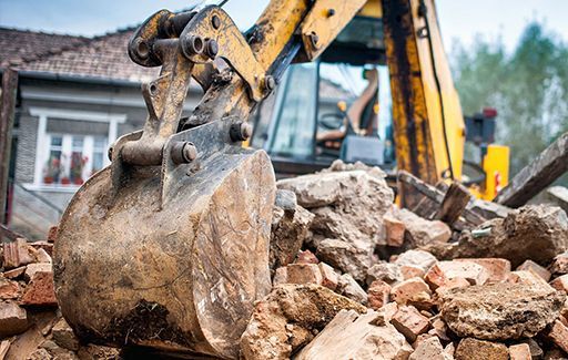 Excavator bucket pushing rubble at a demolition site with broken concrete and debris