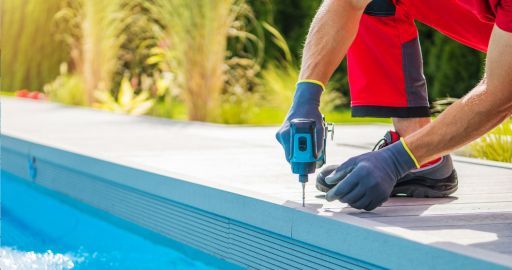 Worker using a blue drill to install a pool deck beside a swimming pool