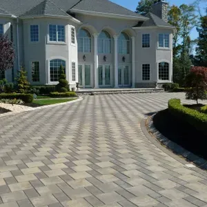 Large beige mansion with arched windows and a patterned stone driveway under a clear blue sky