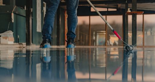 Workers mopping a glossy floor in an unfinished room, with reflections visible.