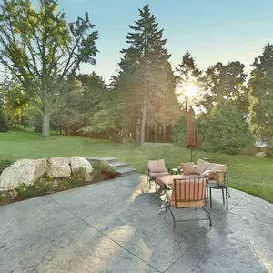 Patio seating area on a concrete patio with lawn, trees, and low sun shining through the backyard.