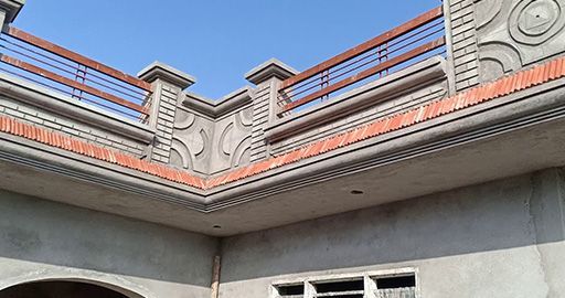 House roofline with decorative gray railings and orange trim against a blue sky