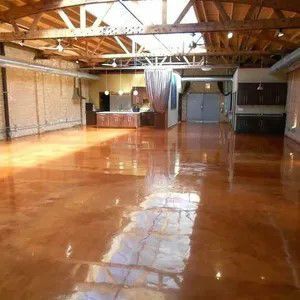 Empty loft with polished concrete floor, exposed wooden beams, and a small bar area in the back.