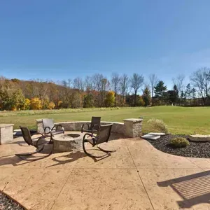 Patio with metal chairs and fire pit overlooking a grassy yard and trees under a clear blue sky