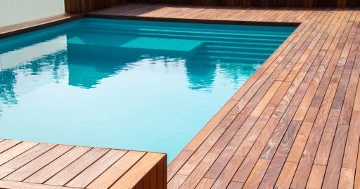 Wooden deck surrounding a clear blue swimming pool with turquoise water reflections