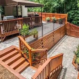 Multi-level wooden deck with stairs, railings, potted plants, and stone patio in a wooded backyard