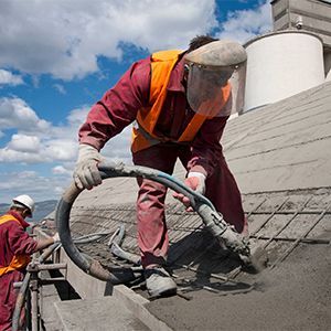 Workers in safety gear spraying coating on a rooftop under a blue sky