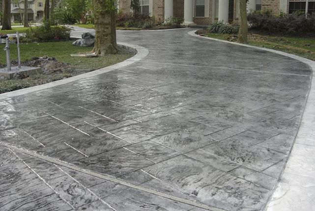 Wet stamped concrete driveway curving past landscaped greenery and a building entrance