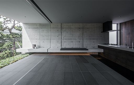 Minimalist modern patio with concrete walls, dark tile floor, and built-in benches overlooking greenery