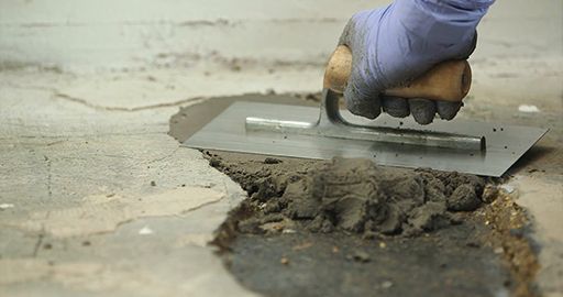 Gloved hand spreading mortar over a damaged concrete surface with a trowel