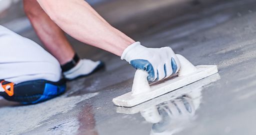 Person using a white trowel to smooth wet concrete on a floor outdoors