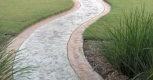 Curved concrete garden path bordered by grass and tall plants