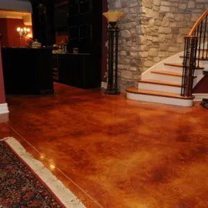 Polished stained concrete floor in a home interior with a staircase and stone wall backdrop
