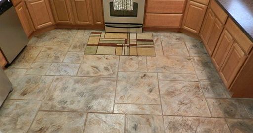Kitchen floor with tan tile and a small patterned rug in front of the stove and cabinets