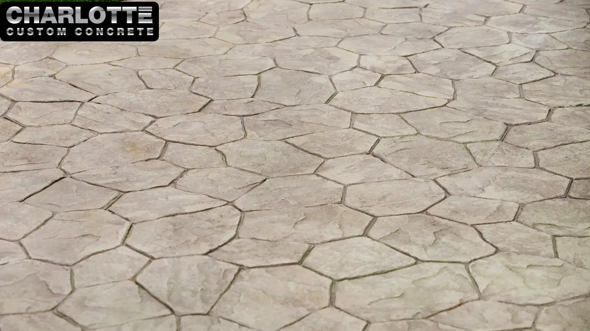 Cracked beige stone pavement with irregular polygon tiles and a Charlotte Custom Concrete logo in the corner