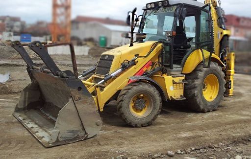 Yellow backhoe loader with front bucket parked on a dirt lot near construction equipment