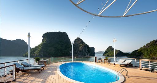 Infinity pool on a deck overlooking a calm sea and rocky green islands under a clear blue sky