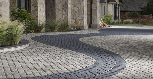 Curved cobblestone driveway beside a stone building and landscaped planter.