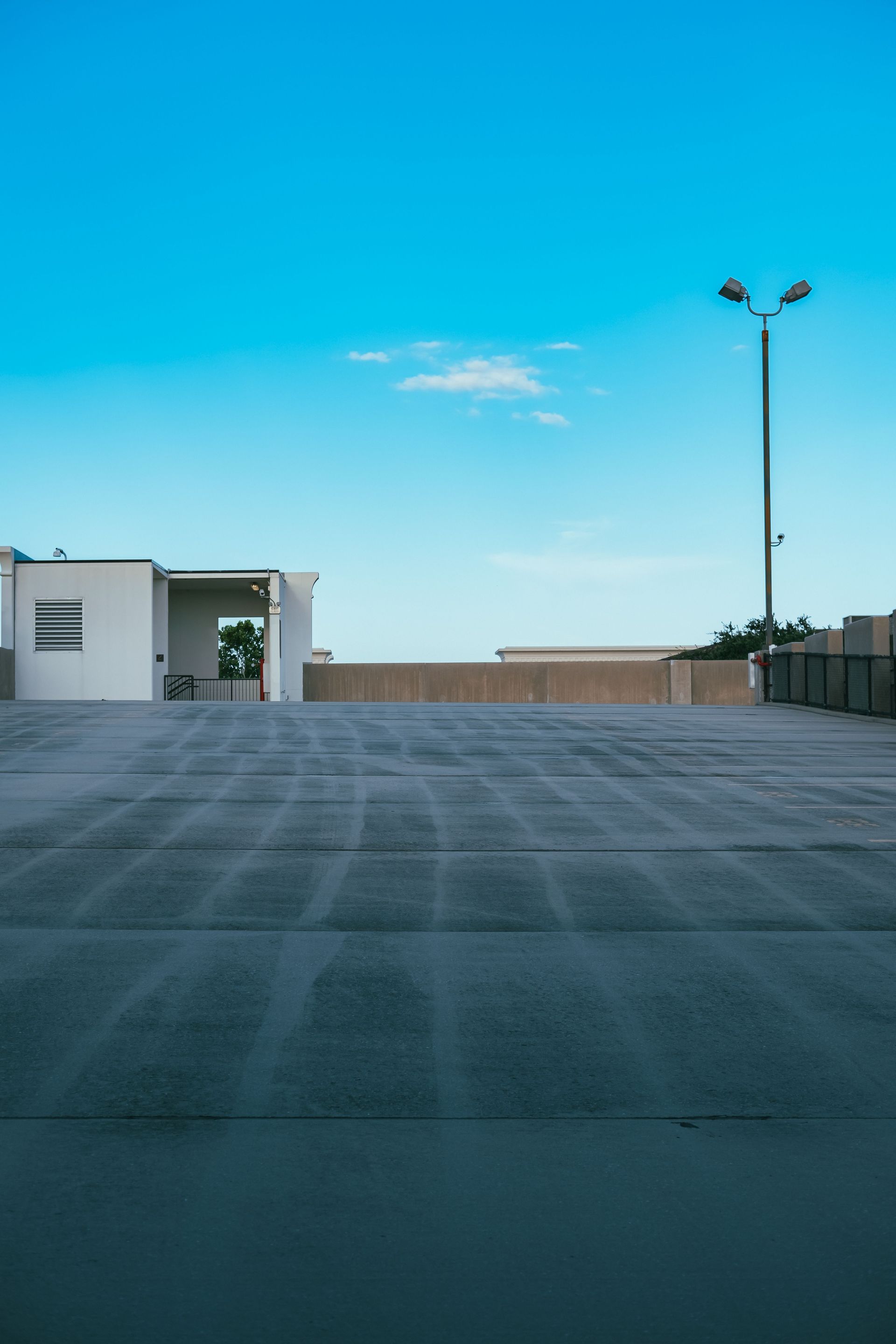 Empty rooftop parking lot under a clear blue sky, with a white building and streetlights in the distance