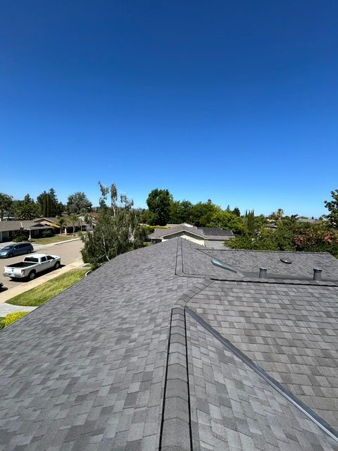 Gray shingled roof with a clear blue sky background. Surrounding trees and houses.