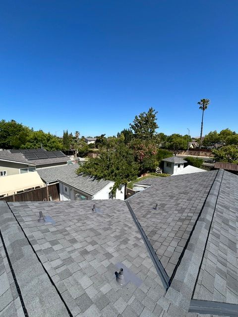 View from a roof, showing gray shingled roofs of houses against a clear blue sky.