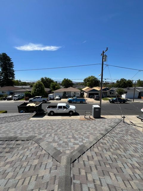 Overhead view of a suburban street with houses, a white truck, and a rooftop in the foreground, under a bright blue sky.