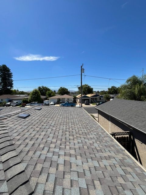 View of a shingled roof with a clear blue sky and neighborhood in the background.