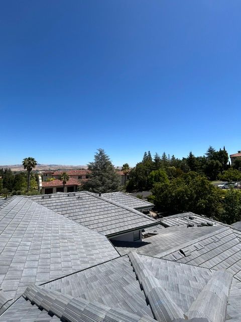 View of a gray tiled roof with a clear blue sky and trees in the background.