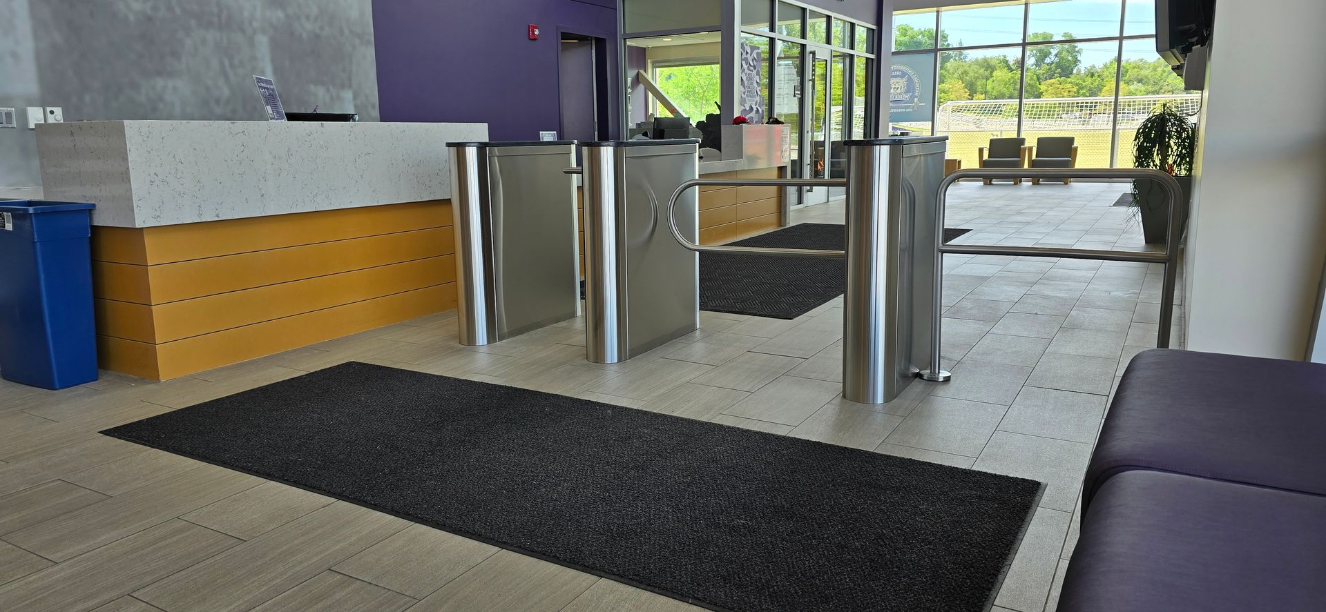 Turnstiles in a building entrance, with a reception desk and a window view.