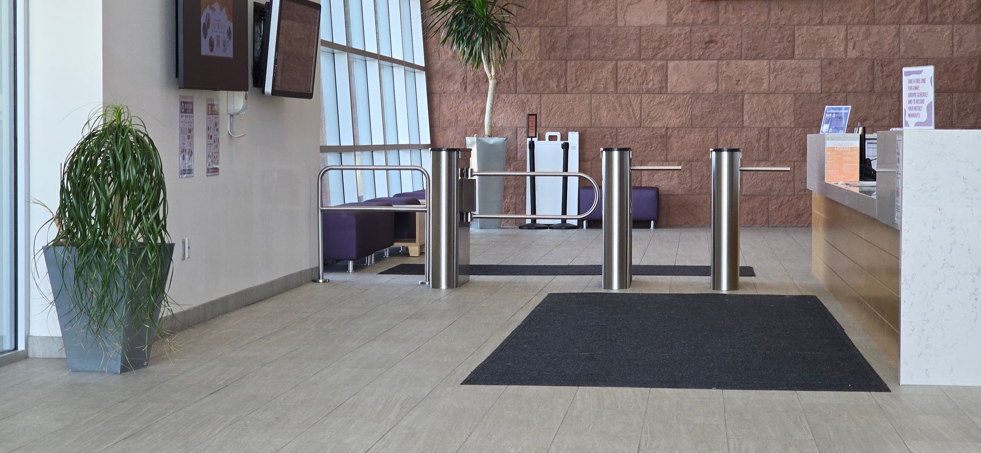 Entrance to a building with turnstiles, reception desk, and potted plants.