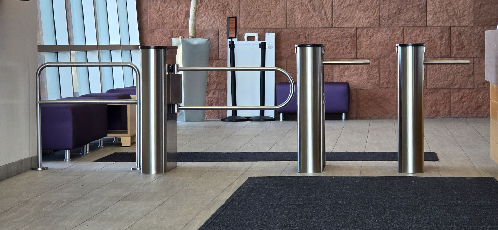 Stainless steel turnstiles in a building entrance, set on a dark mat.