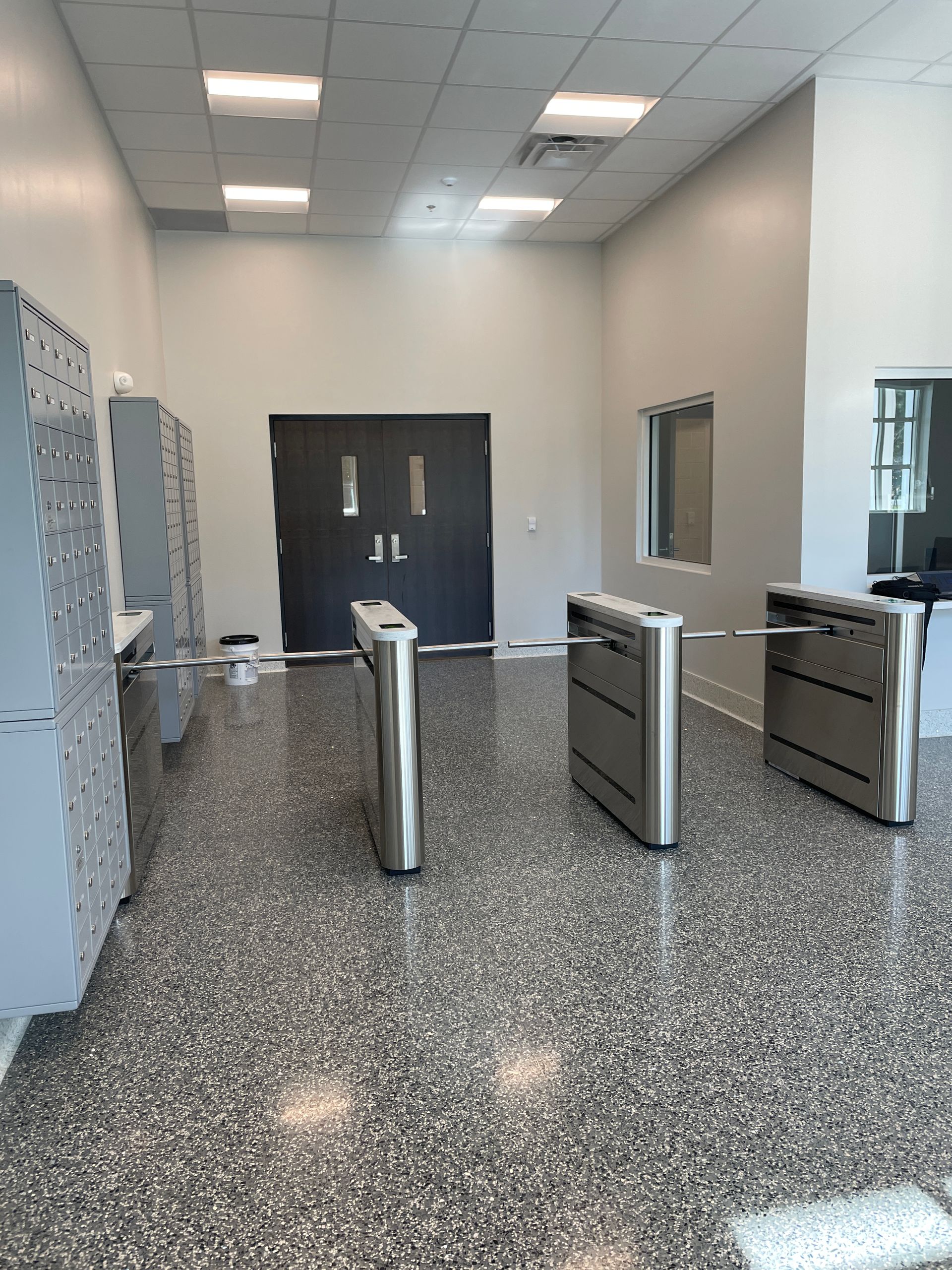 Lobby with a gray speckled floor, turnstiles, and a locked black door. 