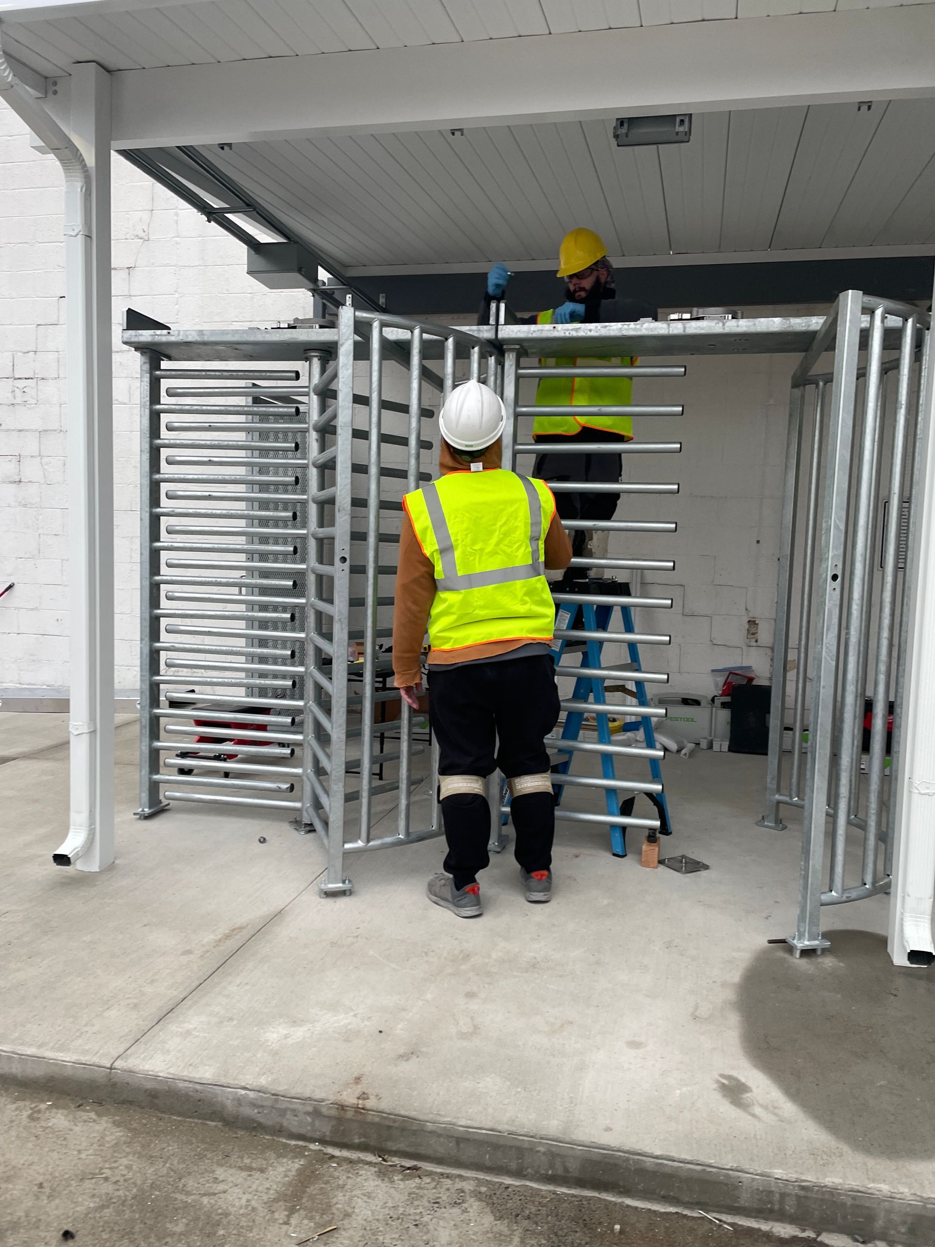Workers installing a metal turnstile under a white awning. 