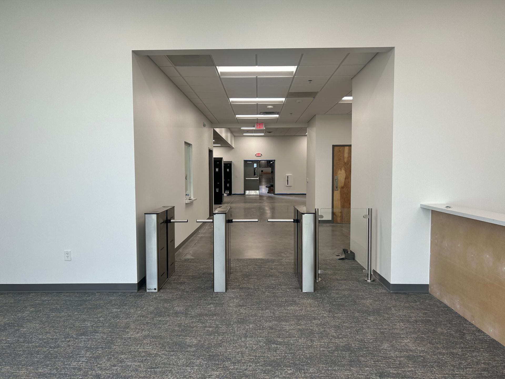 Entrance to a building with turnstiles and a long hallway, gray carpet and white walls.