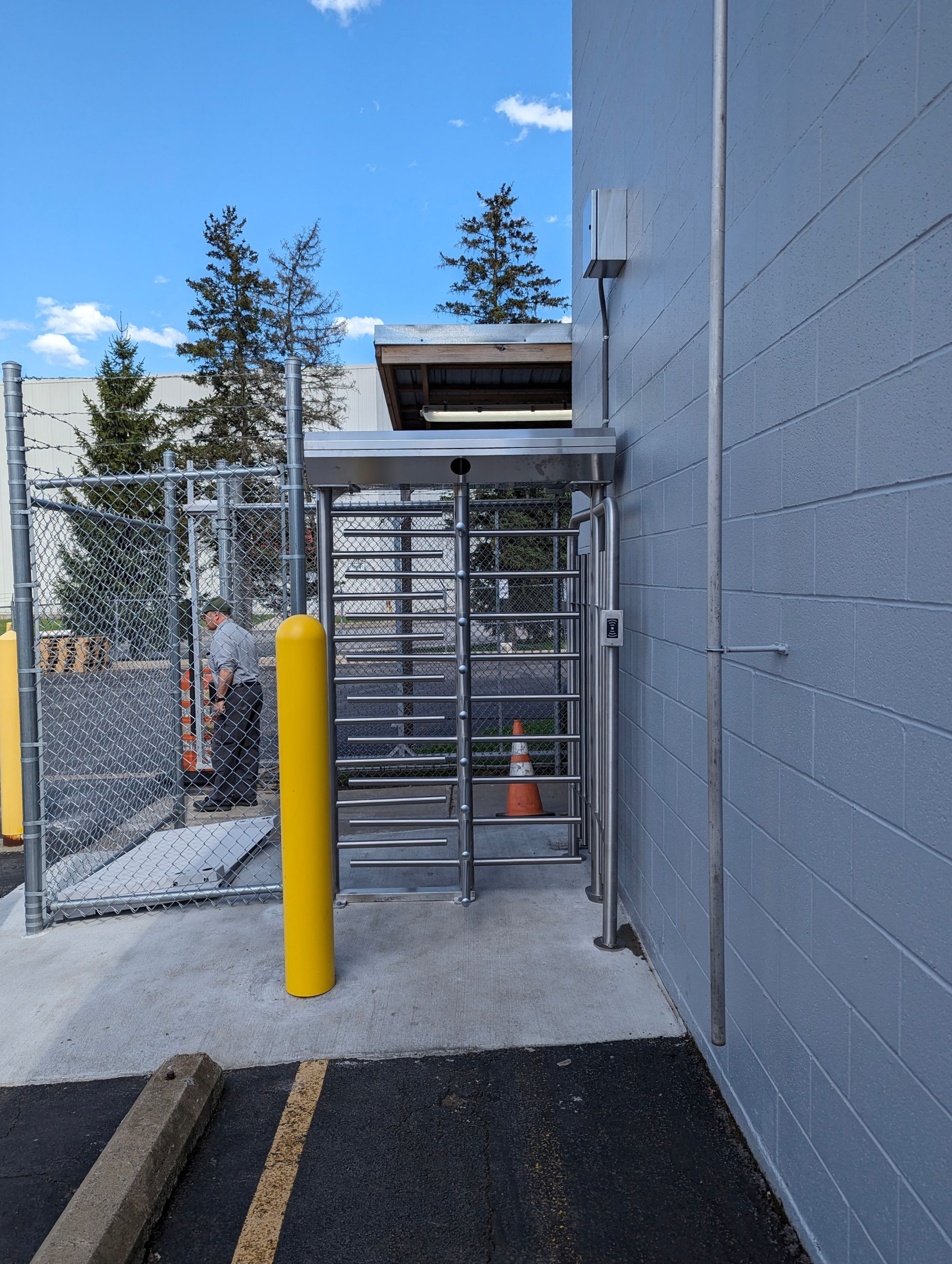 Turnstile security entrance next to a gray building and chain-link fence.