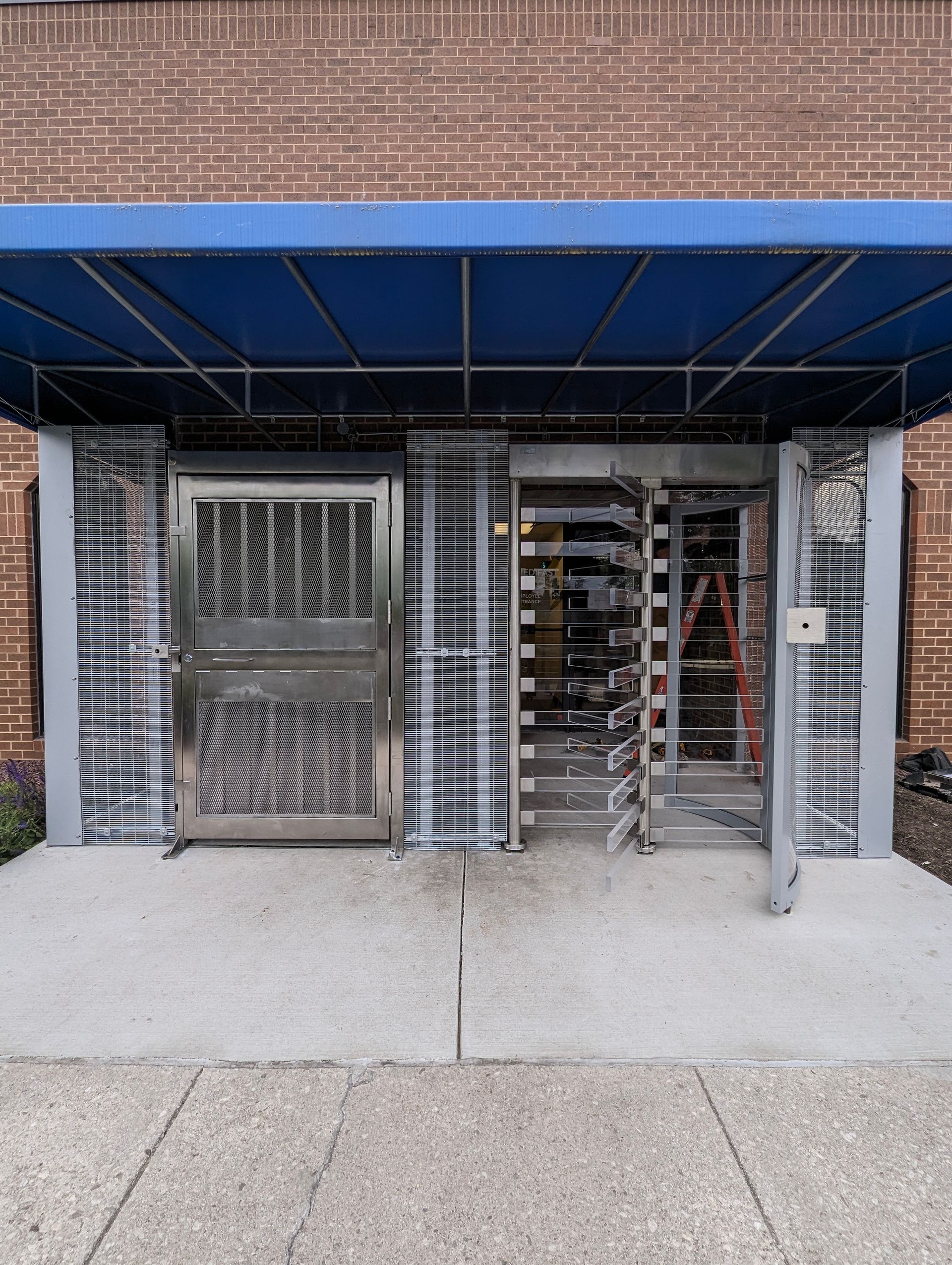 Building entrance with blue awning, stainless steel door, and revolving door on a concrete path.
