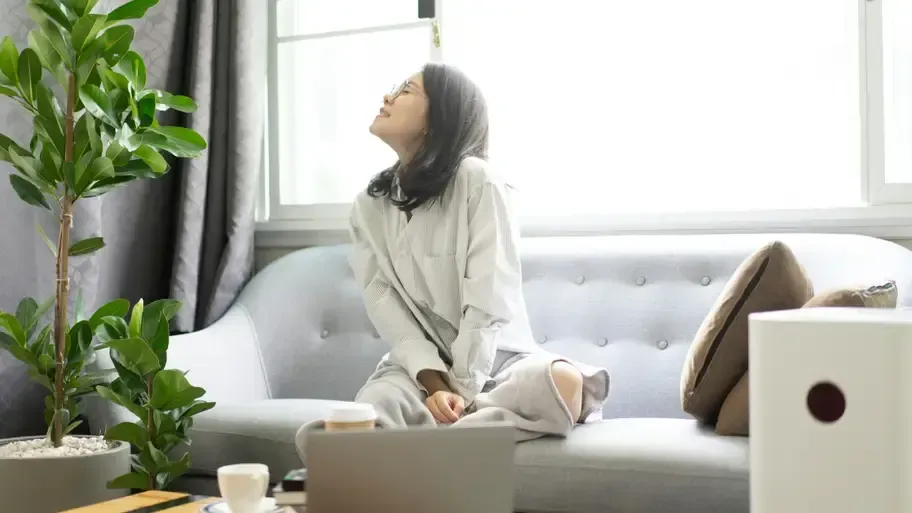 A woman is sitting on a couch in a living room with a laptop.