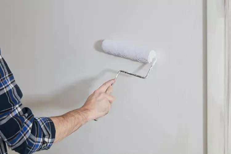 A man is painting a wall with a paint roller.