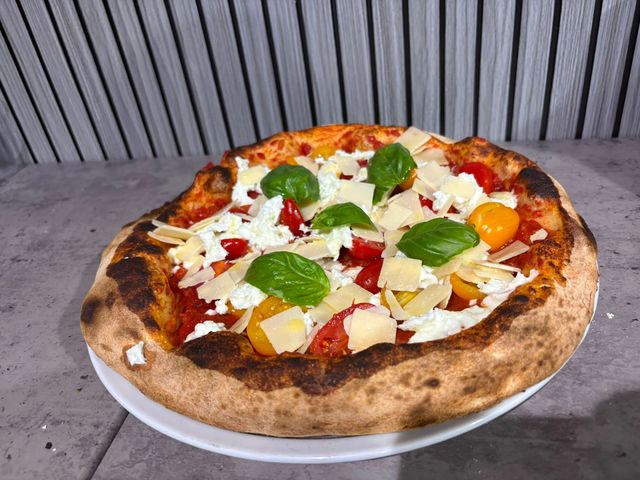 Una pizza napoletana condita con basilico, formaggio, pomodori e frutta su un piatto bianco.