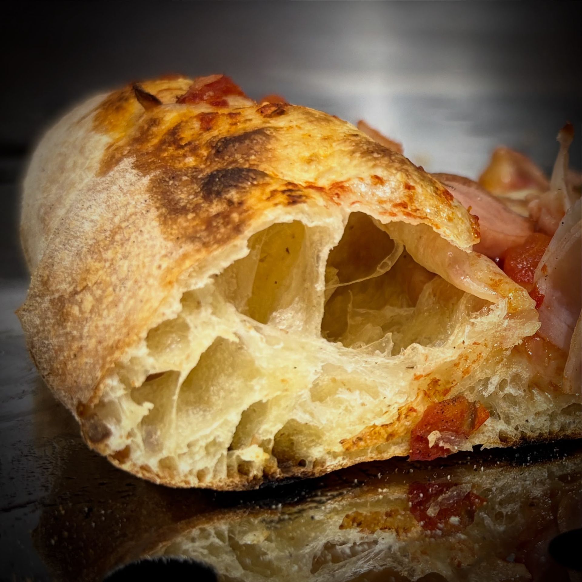 Primo piano di una baguette tagliata a fette, di colore marrone dorato e dalla mollica soffice, su una superficie scura e riflettente.