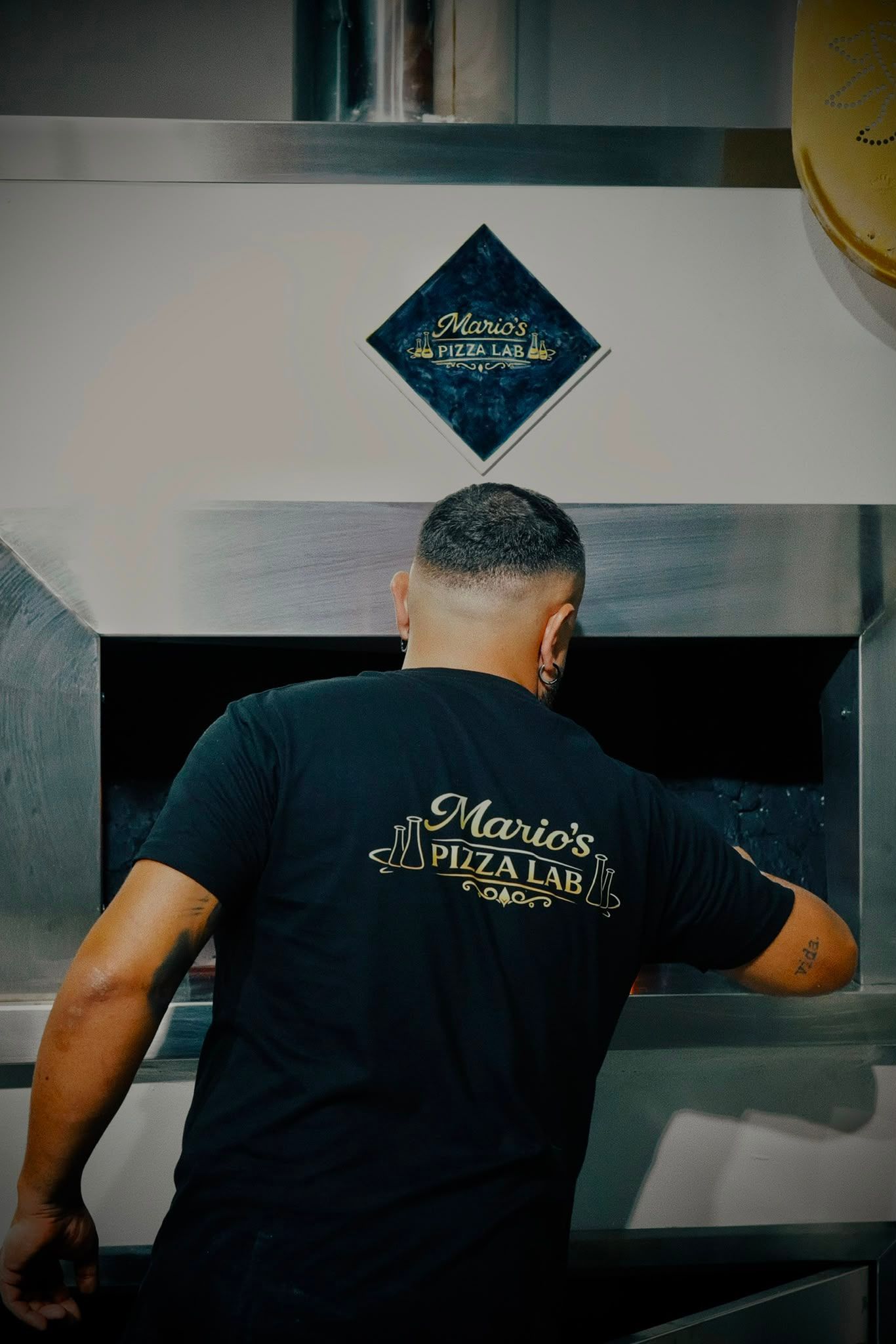 Una persona con una maglietta nera si sporge verso una macchina in acciaio inossidabile con un logo a forma di diamante blu.