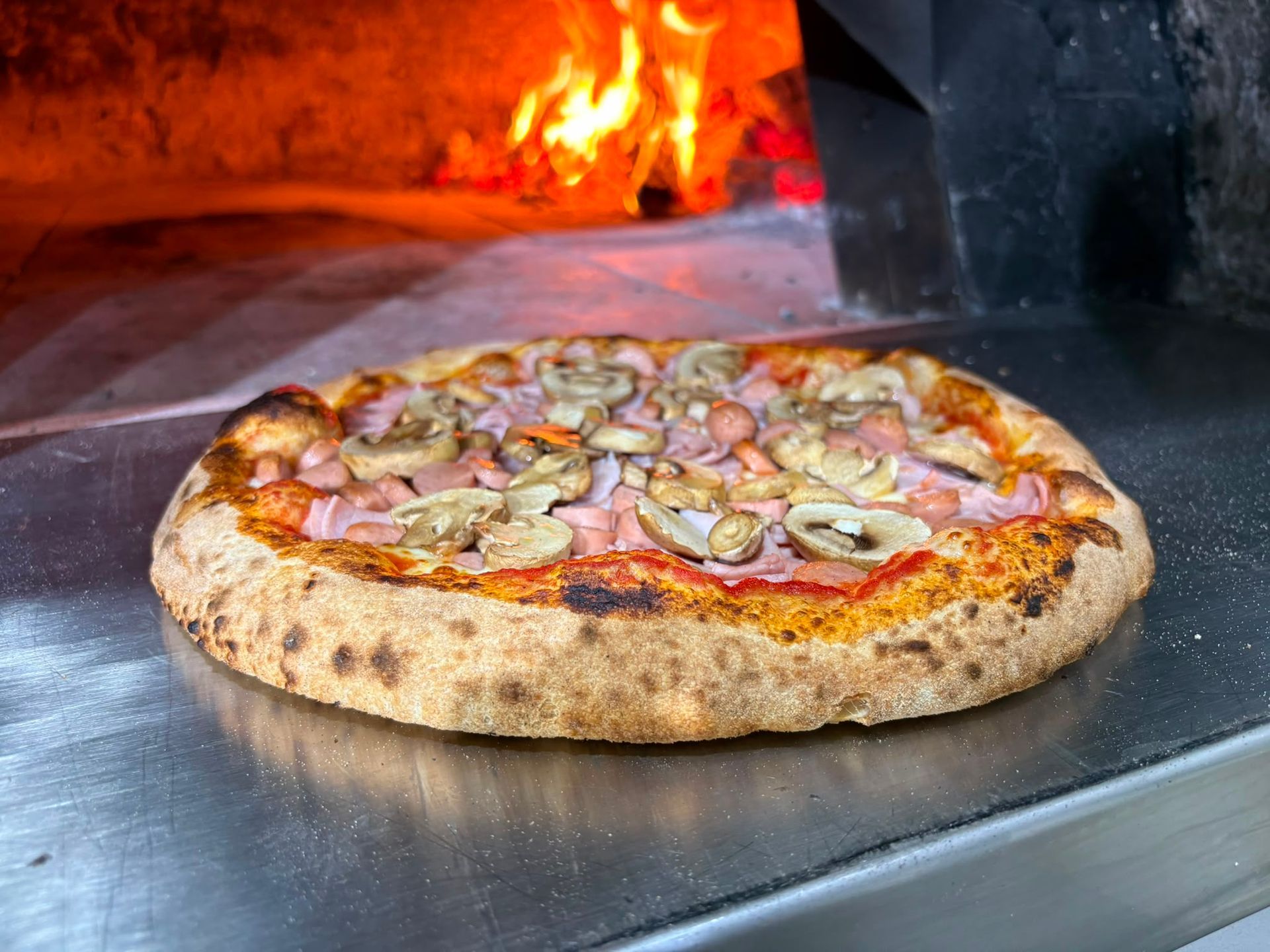 Pizza che cuoce in un forno a legna con le fiamme che brillano alle sue spalle